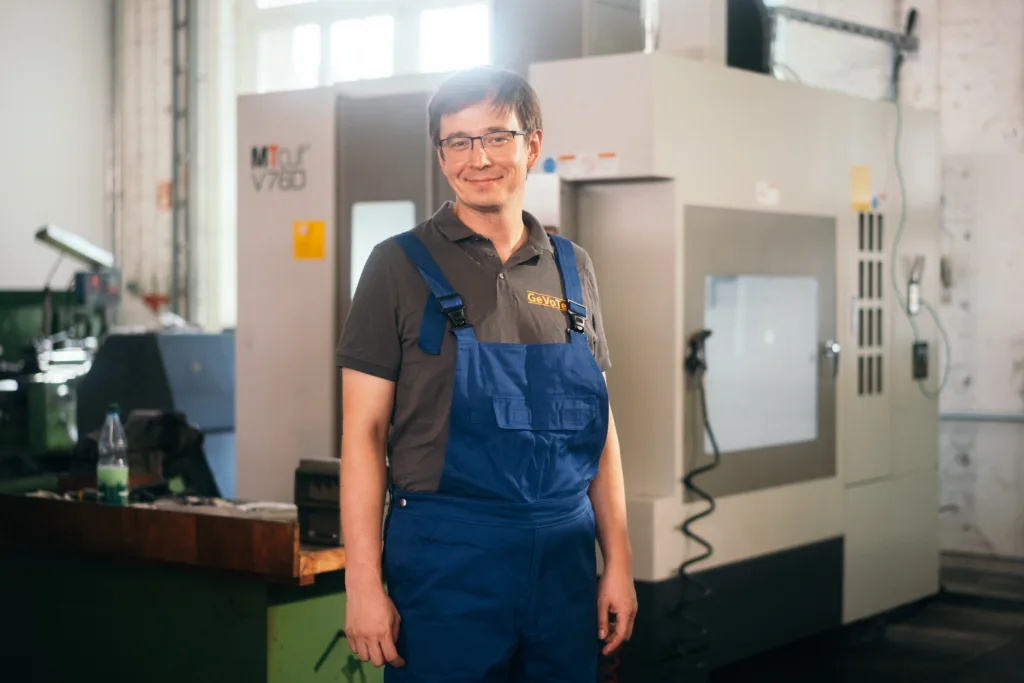 Glimlachende technicus in blauwe overall staat voor een CNC-machine in een werkplaats